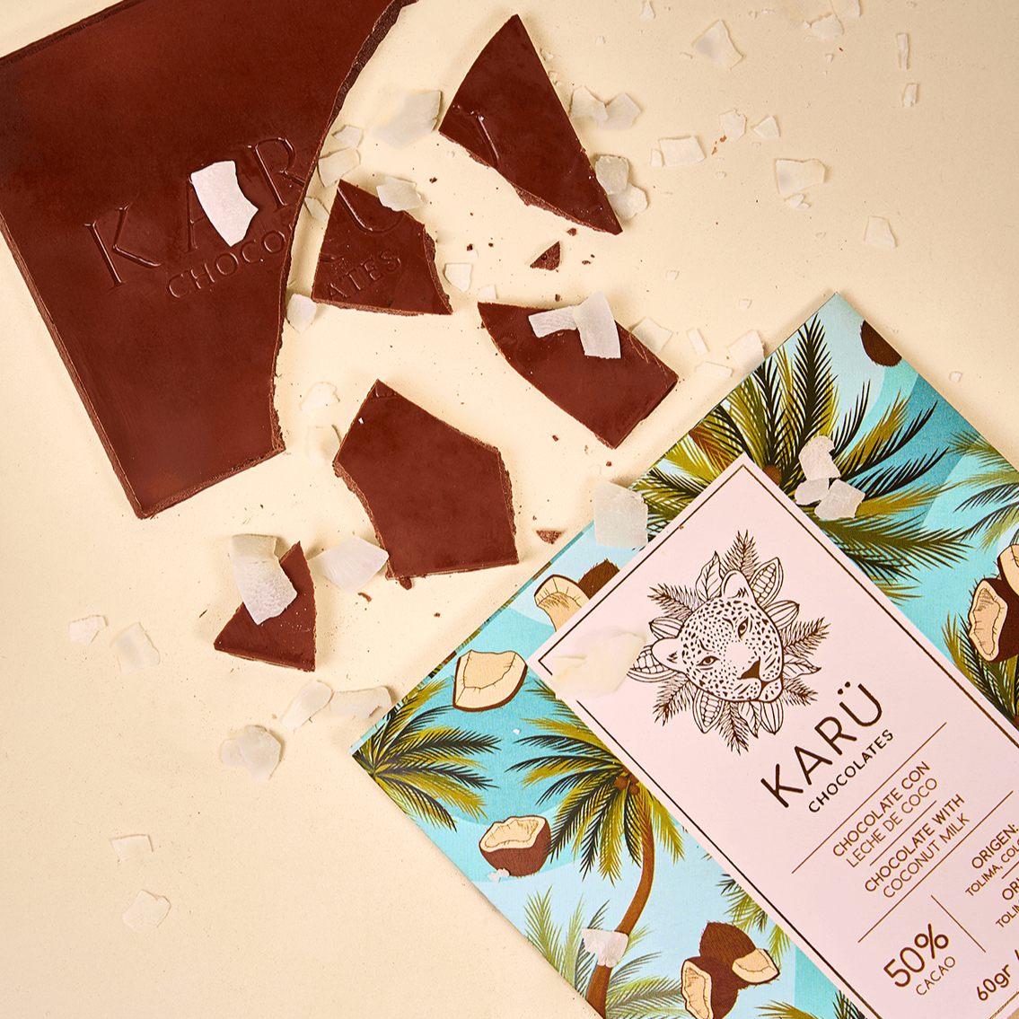Trozos de barra de chocolate con leche de coco Karü, rodeados de virutas de coco, junto a la caja del producto.