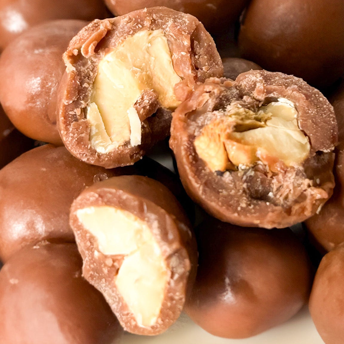 Marañones cubiertos de chocolate Karü sin empaque, con algunos partidos a la mitad mostrando su interior.
